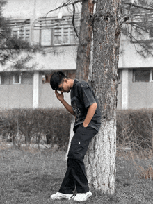 a young man leans against a tree with his head in his hands