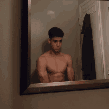 a shirtless young man looks at himself in a mirror