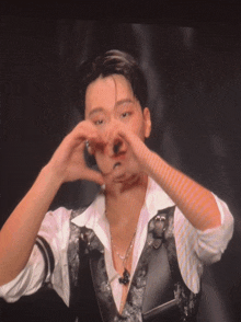 a man in a white shirt and black vest making a heart with his hands