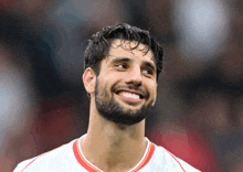 a man with a beard is smiling and wearing a red and white jersey