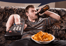 a man sitting on a couch with a remote control and a bowl of chips