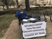 a man sitting at a table with a sign that says xpunks / onxrp have the best discord community