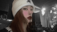 a woman wearing a white beanie is singing into a microphone in a recording studio .