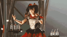a girl in a red and black dress is dancing on a stage with bottles of water in the background .