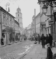 a black and white photo of people walking down a cobblestone street with a sign that says ' leningradska '