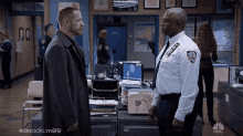 two police officers are standing next to each other in a police station and talking to each other .