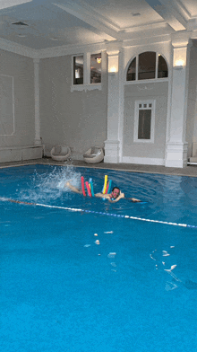 a person is swimming in a large indoor pool with foam noodles