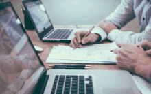 a group of people are sitting at a table using laptops and papers .