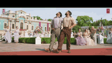 two men are dancing on a red carpet in front of a building that has a red sign on it