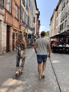 a man and a woman walk down a cobblestone street in front of a store that says ' coca cola ' on the front