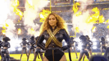 a woman in a black and gold outfit is standing in front of a group of cheerleaders on a football field .