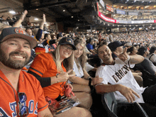 a group of people sitting in a stadium with one wearing an astros shirt