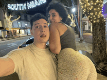 a man and a woman are posing for a picture in front of a sign that says south miami