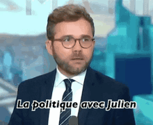 a man in a suit and tie is talking into a microphone and the words la politique avec julien are above him .