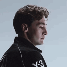 a man with curly hair is wearing a black jacket with the letters y3 on the sleeve .