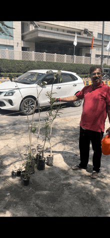 a man in a red shirt is holding a watering can in front of a white car