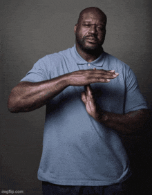 a man in a blue shirt has his hands folded in front of his face