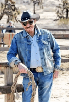 a man wearing a cowboy hat and a denim jacket is holding a lasso .