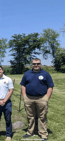 two men are standing in a grassy field with one wearing a blue shirt with a circle on it