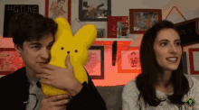 a man holds a yellow stuffed bunny while a woman looks on with a sign above them that says #gtlive