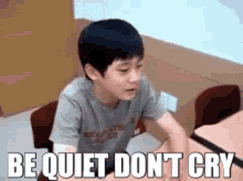 a young boy is sitting at a desk with the words `` be quiet do n't cry '' written on it .