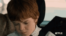 a boy with red hair is sitting in the back seat of a car .