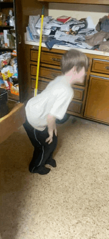 a young boy is standing in front of a dresser with a mop