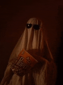 a ghost is wearing sunglasses and holding a bag of popcorn in a dark room .