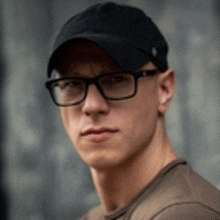 a young man wearing glasses and a baseball cap .