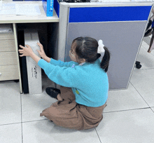 a woman in a blue sweater is kneeling down reaching for a box that says ' samsung ' on the front