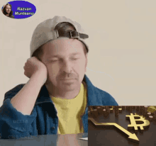 a man sitting at a table with his head resting on his hand next to a display of a graph with a bitcoin symbol on it