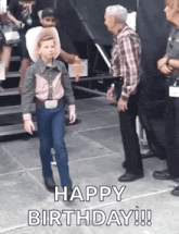a young boy dressed as a cowboy is walking in front of a man .
