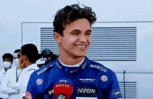 a young man in a racing suit is talking into a microphone and smiling .