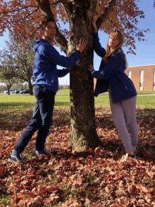 a boy and a girl hugging a tree in a park