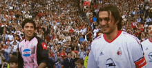 two soccer players are walking in front of a crowd with one wearing a pink shirt that says coca cola