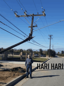 a man standing on the side of a road next to a power pole that has fallen