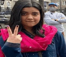 a woman in a pink scarf is giving a peace sign with her fingers .