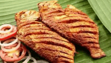 two fried fish are sitting on top of a banana leaf with tomatoes and onions .