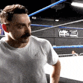 a man in a white shirt stands in a boxing ring with a nyc banner hanging on the wall behind him