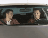 two men are sitting in a car laughing and smiling