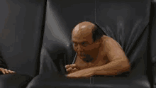 a bald man is sticking his head through a hole in a black leather chair .