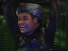 a man wearing a fur hat is laughing and waving his arms
