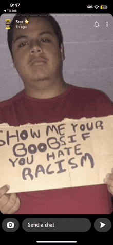 a man in a red shirt is holding a sign that says show me your boobs if you hate racism