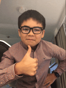 a young boy wearing glasses and a watch giving a thumbs up