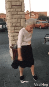 an elderly woman is dancing in front of a brick wall with the words yay written below her