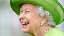 queen elizabeth wearing a green hat and pearl earrings smiles