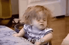 a little girl with messy hair is sitting on a couch and says `` so tired '' .
