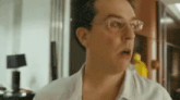 a man wearing glasses is making a surprised face in a room .
