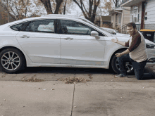 a man kneeling in front of a white car with a yellow trash can that says recycling