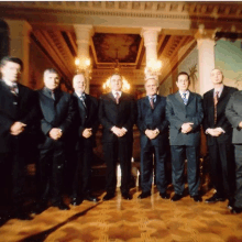 a group of men in suits and ties pose for a photo in a hallway